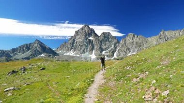     Kadın çiçek yeşil çayır yüksek irtifa kayalık dağ ve tepeler arasında geçiş patika üzerinde pastoral dağ manzarası içinde trekking. İtalyan Alpleri maceralara yaz. 