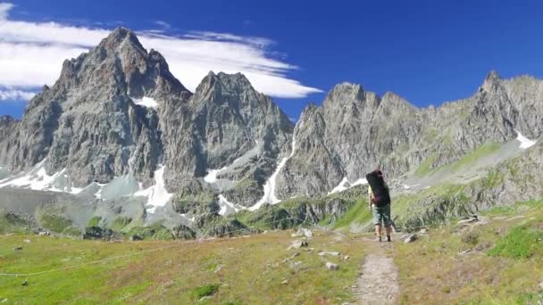 Mujer trekking en idílico paisaje de montaña en el sendero cruzando floreciente prado verde situado en medio de alta altitud cordillera rocosa y picos. Aventuras de verano en los Alpes italianos . — Vídeo de stock