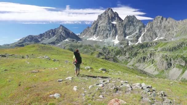 Wanderin in idyllischer Berglandschaft auf einem Fußweg über blühende grüne Wiesen inmitten hoher felsiger Gebirgsketten und Gipfel. Sommerabenteuer auf den italienischen Alpen. — Stockvideo