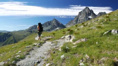 Kadın çiçek yeşil çayır yüksek irtifa kayalık dağ ve tepeler arasında geçiş patika üzerinde pastoral dağ manzarası içinde trekking. İtalyan Alpleri yaz maceralara. ağır çekim.