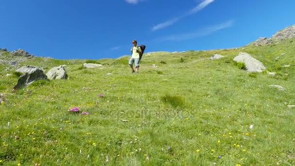 Vrouw wandeltochten in idyllisch berglandschap op voetpad overschrijding van bloeiende groene weide temidden van grote hoogte rotsachtige bergketen en pieken. Zomer avonturen op de Italiaanse Alpen. Slow motion. — Stockvideo