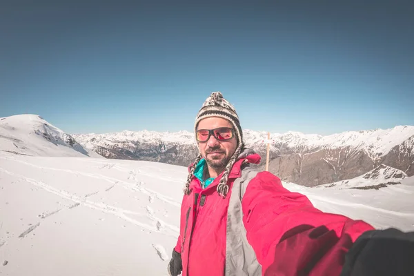 Adult alpin skier with beard, sunglasses and hat, taking selfie on snowy slope in the beautiful italian Alps with clear blue sky. Concept of wanderlust and adventures on the mountain. Wide angle fishe — Stock Photo, Image