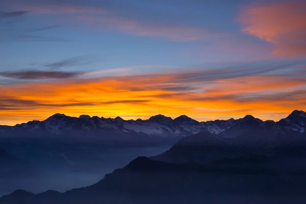 Colorida luz del sol detrás de majestuosas cumbres montañosas de los Alpes italianos-franceses, vistas desde lejos. Niebla y niebla que cubre los valles de abajo, paisaje otoñal, sensación de frío . — Foto de Stock