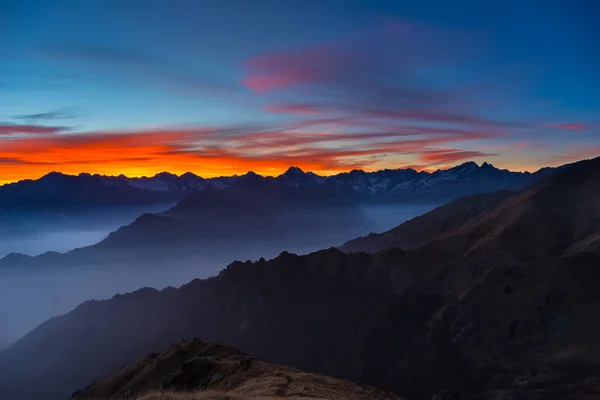 从远处看七彩阳光背后的意大利-法国阿尔卑斯山，雄伟的山峰。雾和烟雾笼罩的山谷，秋色，阴冷的感觉. — 图库照片