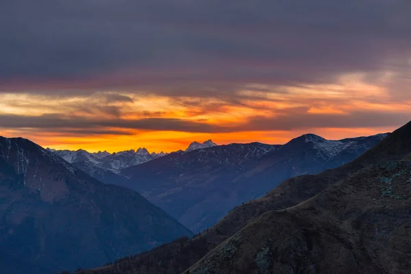 Colorida luz del sol detrás de majestuosas cumbres montañosas de los Alpes italianos-franceses, vistas desde lejos. Niebla y niebla que cubre los valles de abajo, paisaje otoñal, sensación de frío . — Foto de Stock