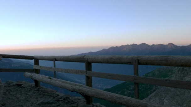 Mann blickt vom Holzbalkon auf die Berge bei Sonnenaufgang und trinkt Heißgetränk aus Becher, hoch oben auf den Alpen. — Stockvideo