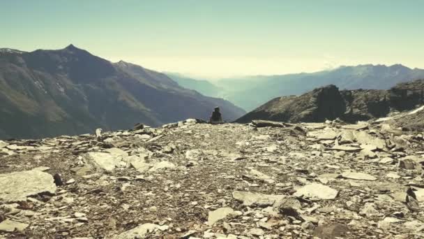 Zeitlupe auf eine einsame Frau, die auf felsigem Gelände sitzt und den weiten Blick über das Tal beobachtet. Sommerabenteuer auf den italienischen Alpen — Stockvideo