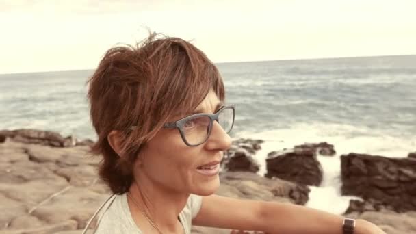 Profil szemüvegek és vörös szőrszálak felnőtt nő portréja. Defocused a háttérben hullámzó óceán. Lassú mozgás, régi retro vintage szűrő. — Stock videók