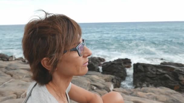 眼鏡と赤い毛の成人女性の横顔の肖像画。海背景にデフォーカスを振っています。スローモーション、古いレトロなビンテージ フィルター. — ストック動画