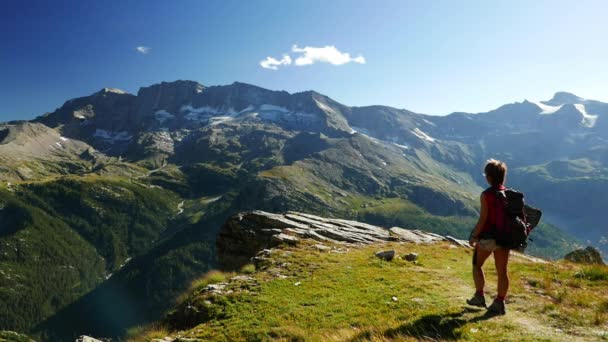 Frau erreicht den Gipfel des Berges in hoher Höhe felsige Landschaft mit Gletscher und Gipfel im Hintergrund. Sommerabenteuer auf den Alpen. Zeitlupe. — Stockvideo