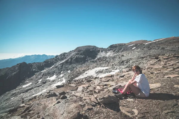 Uma pessoa sentada em terreno rochoso e observando um nascer do sol colorido no alto dos Alpes. Vista de ângulo largo de cima com picos de montanha brilhantes no fundo. Imagem tonificada . — Fotografia de Stock