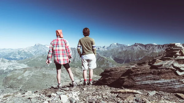 Couple of hiker on the mountain top looking at expasnive view and mountain peaks. Summer adventures on the Alps. Wide angle view from above, toned image, rear view. — Stock Photo, Image