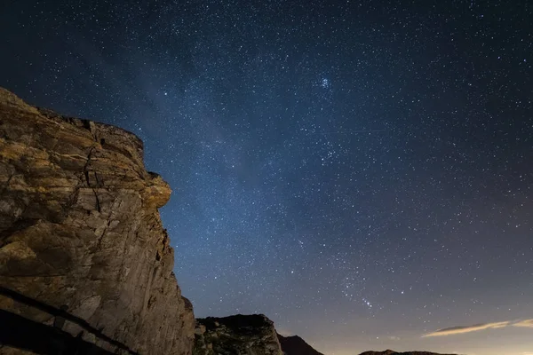 Noche en los Alpes bajo el cielo estrellado y los majestuosos acantilados rocosos en los Alpes italianos, con la constelación de Orión en el horizonte . — Foto de Stock
