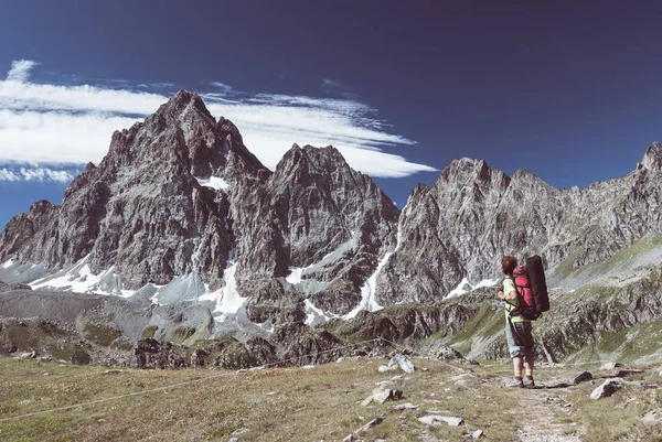 Jeden člověk při pohledu na majestátní pohled zářící horské vrcholy při západu slunce vysoko v Alpách. Pohled zezadu, tónovaný a filtrovaného obrazu, zaostření na pozadí. — Stock fotografie