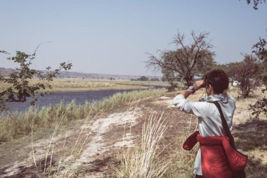 Tourist watching wildlife by binocular on Chobe River, Namibia Botswana border, Africa. Chobe National Park, famous wildlilfe reserve and upscale travel destination. Toned image. clipart