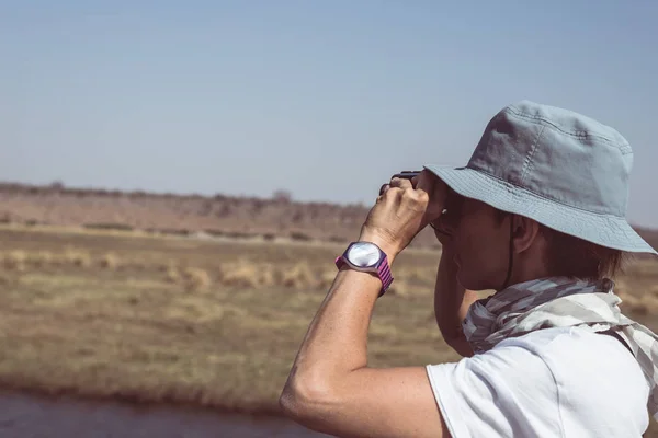 Turista assistindo vida selvagem por binocular em Chobe River, Namíbia Botswana fronteira, África. Chobe National Park, famosa reserva de vida selvagem e destino de viagem de luxo. Imagem tonificada . — Fotografia de Stock