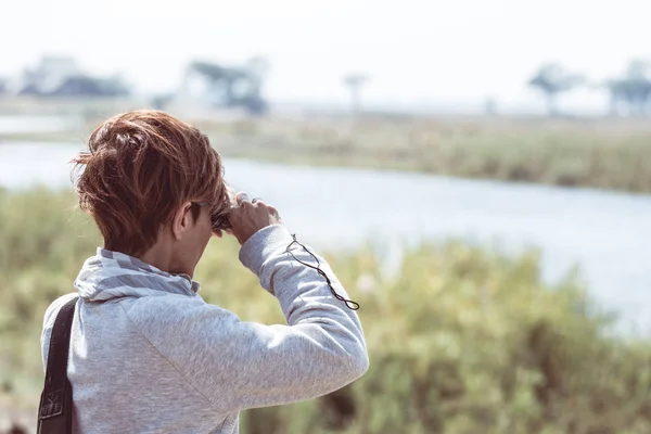 Tourist watching wildlife by binocular on Chobe River, Namibia Botswana border, Africa. Chobe National Park, famous wildlilfe reserve and upscale travel destination. Toned image. — Stock Photo, Image