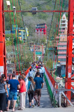Rishikesh, Hindistan - 10 Şubat 2017: Hindu din için Rishikesh, Hindistan, kutsal şehir ve Yoga dersleri için ünlü hedef asma yaya köprüsü üzerinde Ganj nehri geçerken insanlar.