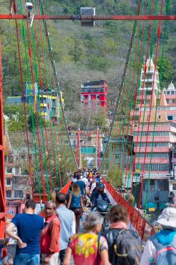 Rishikesh, Hindistan - 10 Şubat 2017: Hindu din için Rishikesh, Hindistan, kutsal şehir ve Yoga dersleri için ünlü hedef asma yaya köprüsü üzerinde Ganj nehri geçerken insanlar.