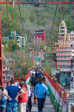 Rishikesh, Hindistan - 10 Şubat 2017: Hindu din için Rishikesh, Hindistan, kutsal şehir ve Yoga dersleri için ünlü hedef asma yaya köprüsü üzerinde Ganj nehri geçerken insanlar.