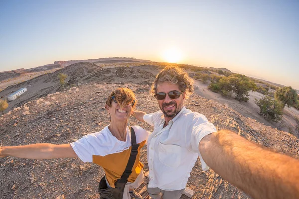 Smiling adult couple taking selfie in the Namib desert, Namib Naukluft National Park, travel destination in Namibia, Africa. Fisheye view in backlight, adventures in Africa.