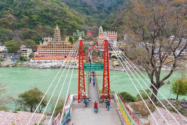 Rishikesh, India - 8 martie 2017: Oamenii care traversează râul Gange pe podul suspendat de la Rishikesh, India, orașul sacru pentru religia hindusă și destinația faimoasă pentru clasele de yoga . — Fotografie, imagine de stoc