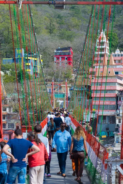 Rishikesh, Hindistan - 10 Şubat 2017: Hindu din için Rishikesh, Hindistan, kutsal şehir ve Yoga dersleri için ünlü hedef asma yaya köprüsü üzerinde Ganj nehri geçerken insanlar.