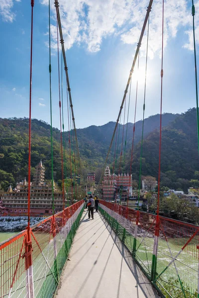 Rishikesh, Hindistan - 10 Şubat 2017: Hindu din için Rishikesh, Hindistan, kutsal şehir ve Yoga dersleri için ünlü hedef asma yaya köprüsü üzerinde Ganj nehri geçerken insanlar.