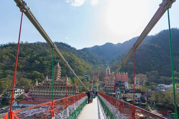 Rishikesh, Hindistan - 10 Şubat 2017: Hindu din için Rishikesh, Hindistan, kutsal şehir ve Yoga dersleri için ünlü hedef asma yaya köprüsü üzerinde Ganj nehri geçerken insanlar. — Stok fotoğraf
