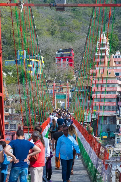 Rishikesh, Hindistan - 10 Şubat 2017: Hindu din için Rishikesh, Hindistan, kutsal şehir ve Yoga dersleri için ünlü hedef asma yaya köprüsü üzerinde Ganj nehri geçerken insanlar.