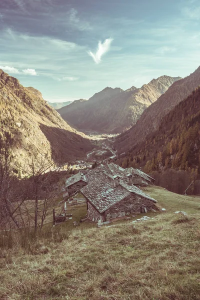 Small group of old stone houses between mountain and forest in the italian Alps. Rural village in valley, toned image, vintage filter. — Stock Photo, Image