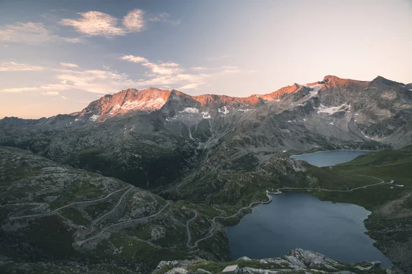 High altitude alpine lake, dams and water basins in idyllic land with majestic rocky mountain peaks glowing at sunset. Wide angle view on the Alps. — Stock Photo, Image