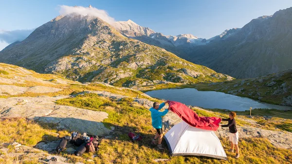 Um par de pessoas montando uma tenda de acampamento nas montanhas, lapso de tempo. Aventuras de verão nos Alpes, lago idílico e cume . — Fotografia de Stock