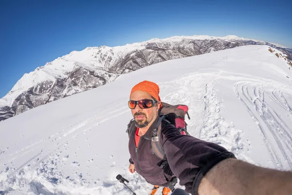 Adult alpin skier with beard, sunglasses and hat, taking selfie on snowy slope in the beautiful italian Alps with clear blue sky. Toned image, vintage style, ultrawide angle fisheye lens. — Stock Photo, Image