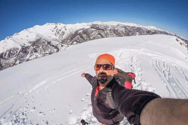 Sciatore adulto alpino con barba, occhiali da sole e cappello, scattando selfie su pendio innevato nelle splendide Alpi italiane con cielo azzurro. Immagine tonica, stile vintage, lente fisheye ultra grandangolare . — Foto Stock