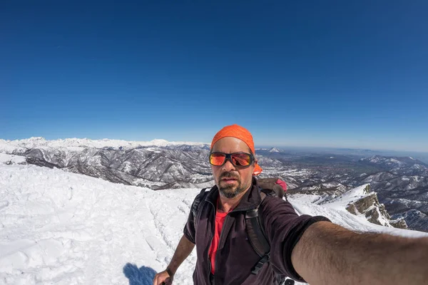 Sciatore adulto alpino con barba, occhiali da sole e cappello, scattando selfie su pendio innevato nelle splendide Alpi italiane con cielo azzurro. Immagine tonica, stile vintage, lente fisheye ultra grandangolare . — Foto Stock