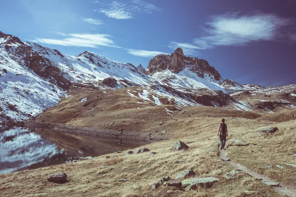 Hiker looking the outstanding view of high altitude landscape and majestic snowcapped mountain peak in autumn season. Wide angle shot in the Italian French Alps. Toned decontrasted image. — Stock Photo, Image