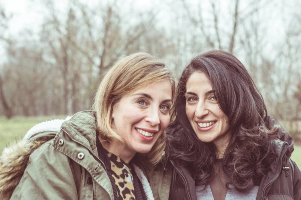Due belle giovani donne che parlano, sorridono e si divertono all'aperto in una fredda giornata autunnale. Luce naturale, pelle naturale, sfondo naturale . — Foto Stock