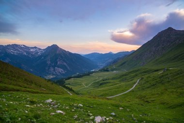 Mountain road leading to high mountain pass on the Italian Alps.. Expasive view at sunset, colorful dramatic sky, adventure road trip in summer. clipart