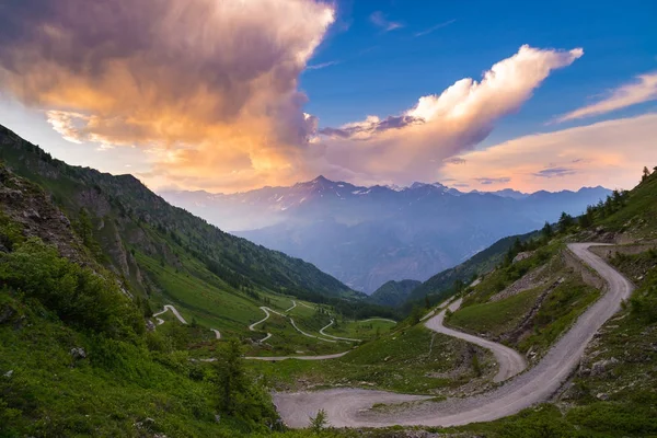 Strada di montagna che conduce al passo di alta montagna sulle Alpi italiane.. Ampia vista al tramonto, cielo colorato drammatico, viaggio avventura su strada in estate . — Foto Stock