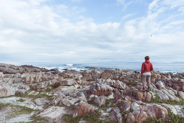 Turista olhando com binocular na linha costeira rochosa em De Kelders, África do Sul, famosa pela observação de baleias. Época de inverno, céu nublado e dramático, imagem tonificada . — Fotografia de Stock