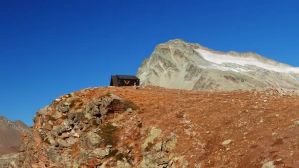 Жінка досягає гірському будиночку зверху у великій висоті скелястий краєвид з льодовик і пік у фоновому режимі. Пригоди на Альпи. — стокове відео