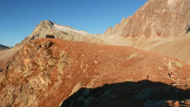 Frau erreicht die Berghütte auf dem Gipfel in hoch gelegener Felslandschaft mit Gletscher und Gipfel im Hintergrund. Abenteuer auf den Alpen. — Stockvideo