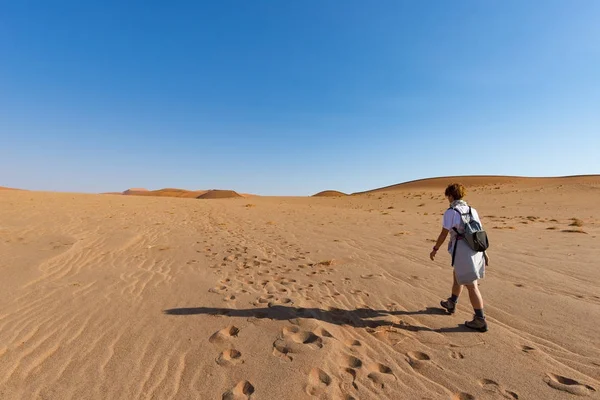 Tourist walking on the sand dunes at Sossusvlei, Namib desert, Namib Naukluft National Park, Namibia. Traveling people, adventure and vacations in Africa.