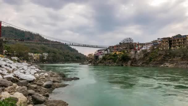 Tempo di crepuscolo a Rishikesh, città santa e destinazione di viaggio in India. Cielo colorato e nuvole in movimento sul fiume Gange. Persone che attraversano il ponte sospeso . — Video Stock