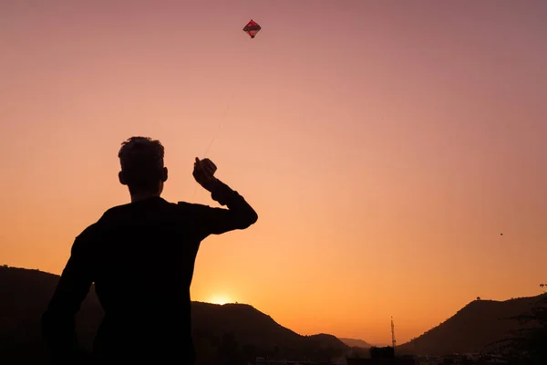 Ung pojke leker med kite vid solnedgången. Bakgrundsbelysning, färgglada himmel, bakifrån, Rajasthan, Indien. — Stockfoto