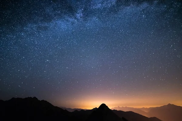 The wonderful starry sky on Christmas time and the majestic high mountain range of the Italian Alps, with glowing villages below. — Stock Photo, Image