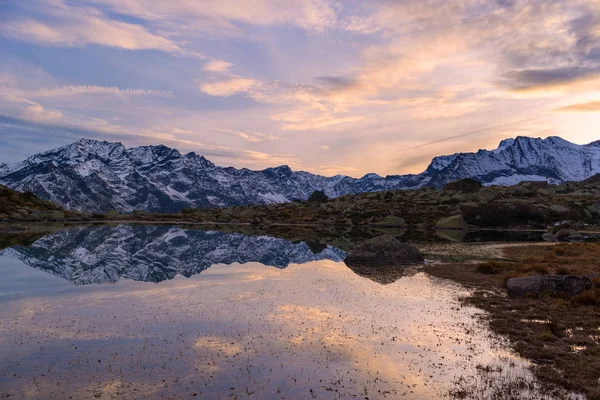 Vysoké nadmořské výšce alpské jezero v idylické krajině. Odraz zasněžené horské pásmo a malebné barevné nebe při západu slunce. Širokoúhlý záběr na Italské Alpy. — Stock fotografie