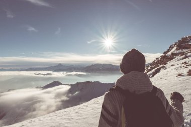 Alpler üzerinde yüksek rütbeli manzaraya bakarak kadın backpacker uzun yürüyüşe çıkan kimse. Görünümü, kış soğuk kar arka, arka ışık yıldızı güneş, bölünmüş tonlama, doygunluğu azaltılmış.