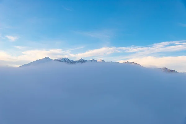 Paisaje alpino escénico, nubes en el valle arisign picos de montaña luz del atardecer, nieve de invierno . —  Fotos de Stock